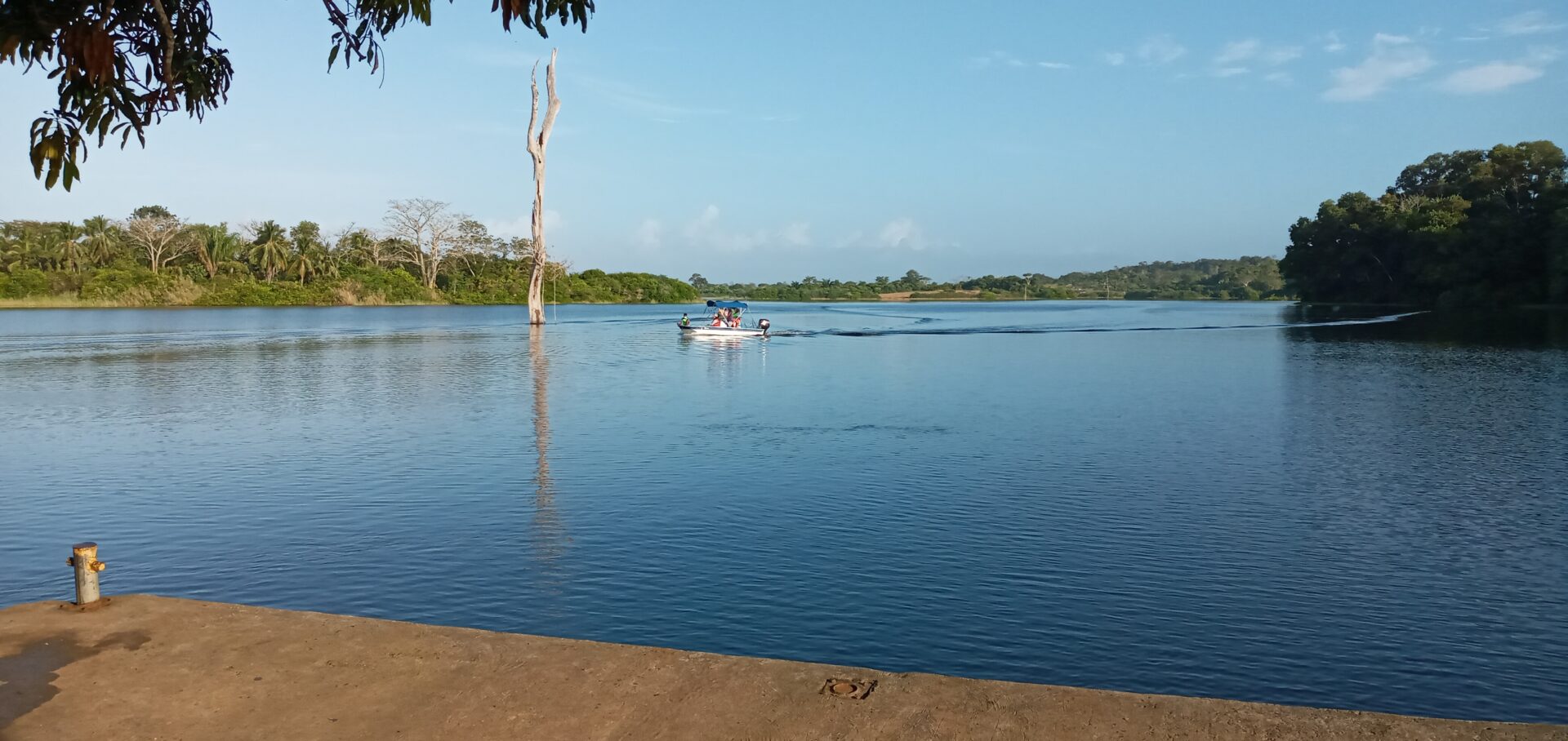 A boat glides on a calm lake with a clear blue sky.