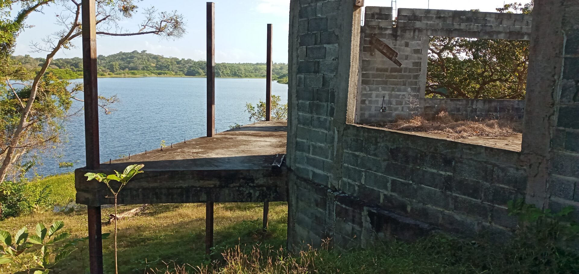 Partially constructed brick building next to a body of water under a clear sky.