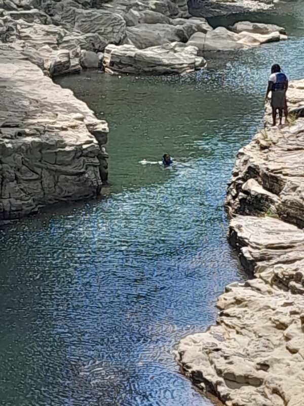 A person swimming in the water near some rocks.
