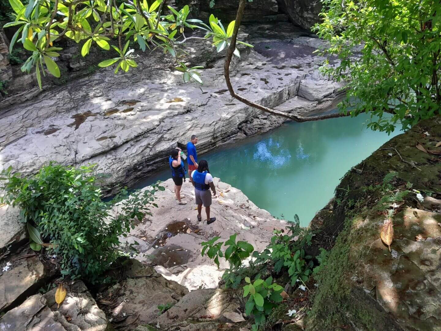 Three people standing on a rock platform near a river.