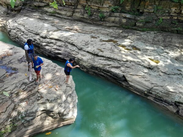 Three people are standing in a river near rocks.