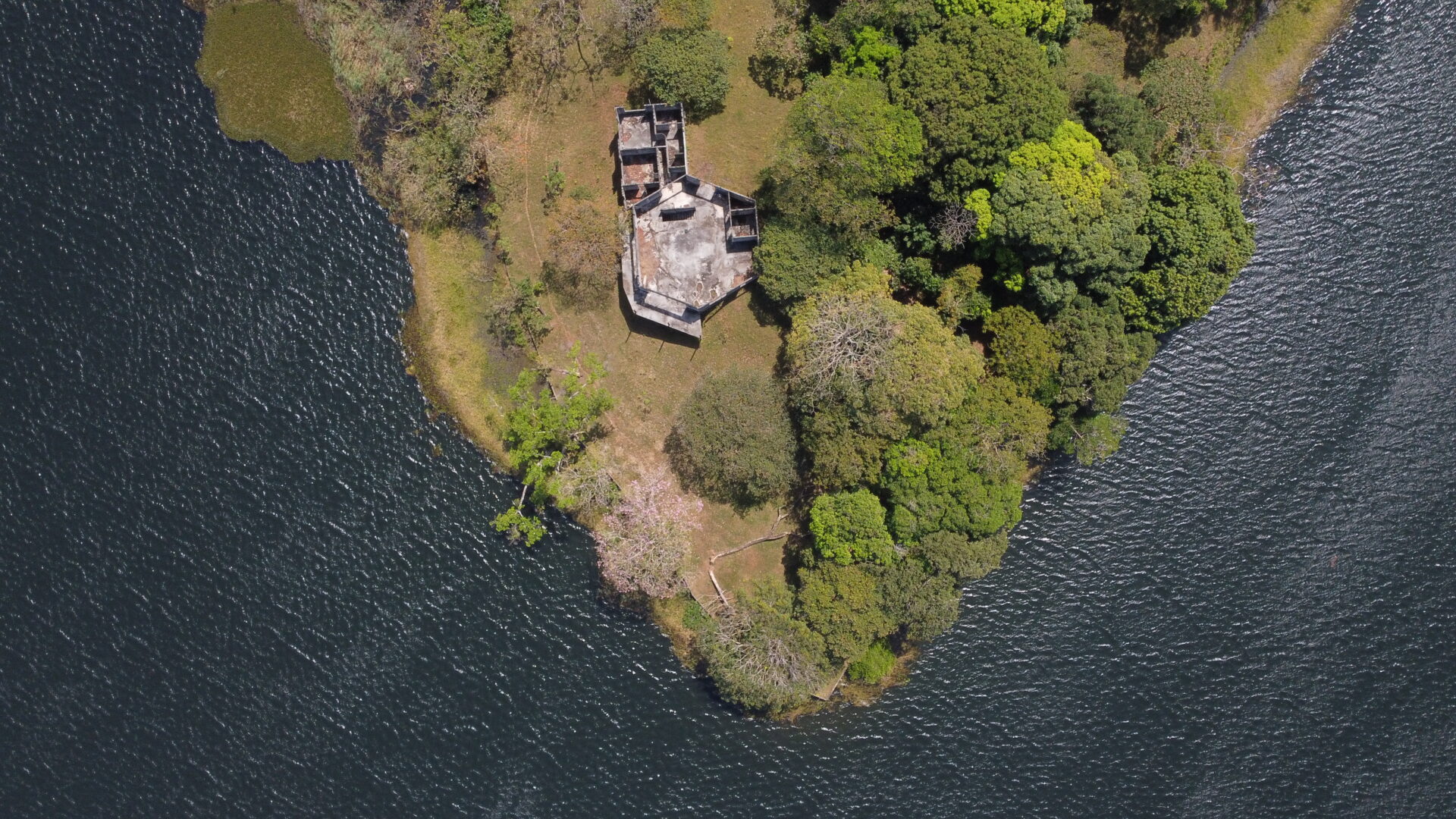 Aerial view of a small island with a ruined building surrounded by trees and water.