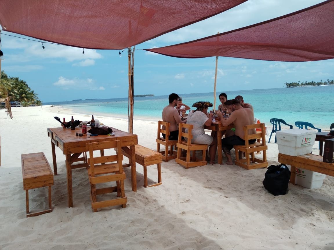 People dining at a beachside restaurant under red canopies.