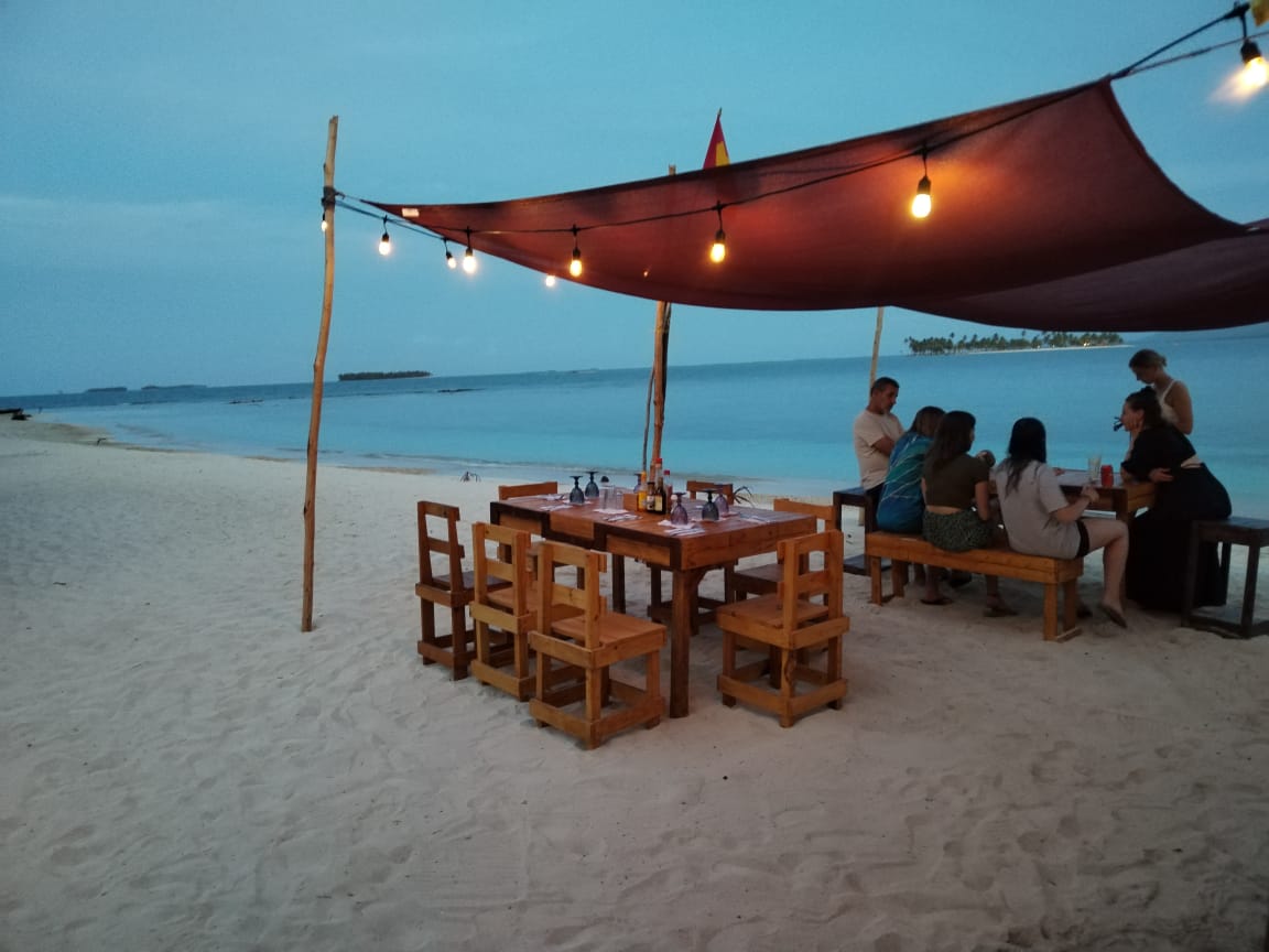 Cozy beachside dining setup with string lights at dusk.