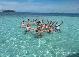 A group of people enjoying in clear ocean water, waving at the camera.