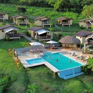 Resort with small cottages and a swimming pool in a lush green area.