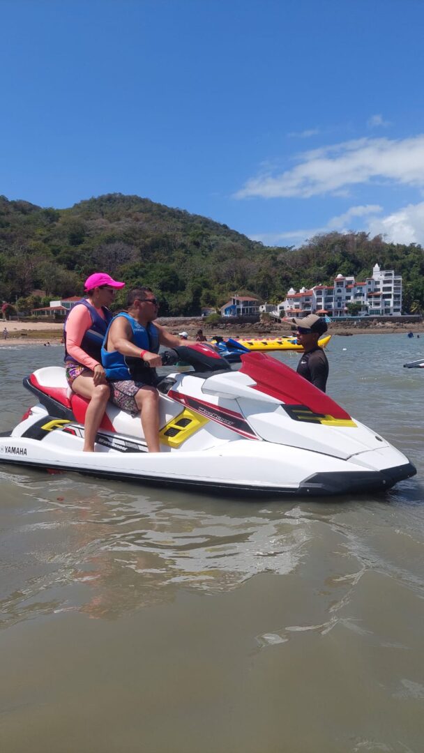 Two people riding a jet ski near the shore with a mountainous backdrop.