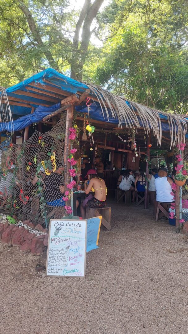 Outdoor rustic cafe with hanging decorations and patrons seated.