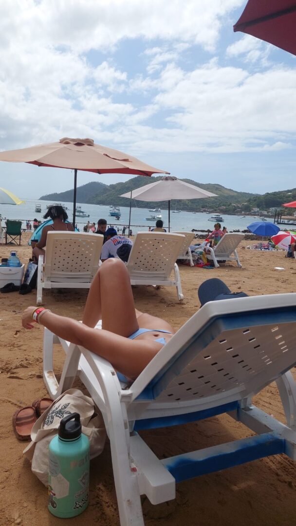 Person relaxing on a beach lounge chair under umbrellas.