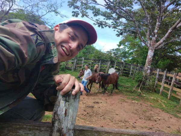 A man leaning on a fence with horses in the background.