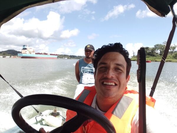 A man in an orange vest driving a boat.