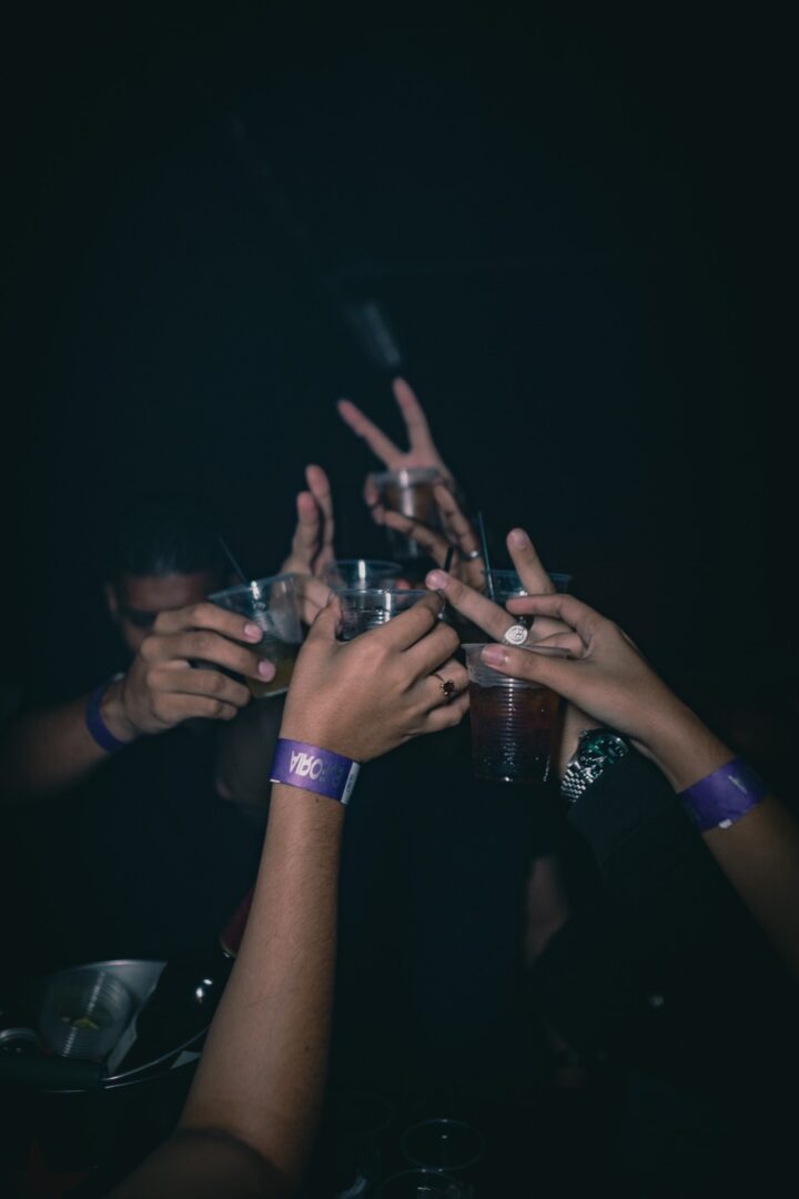 Hands raised with drinks, celebrating in a dark setting.
