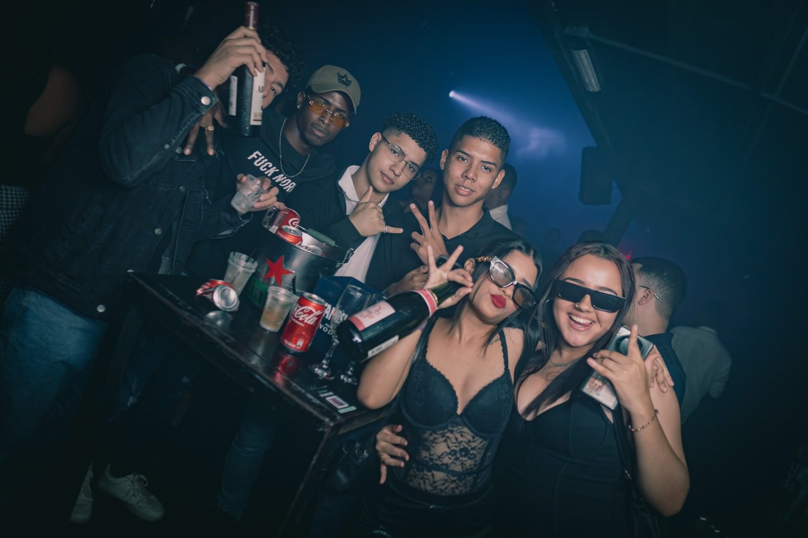 Group of friends enjoying a night out with drinks and sunglasses indoors.