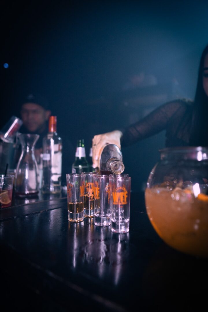 A bartender pours tequila into shot glasses at a dimly lit bar.