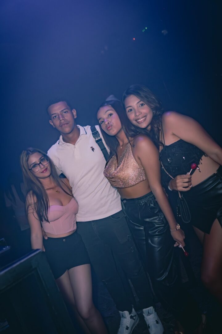 Four friends posing together in a dimly lit party environment.