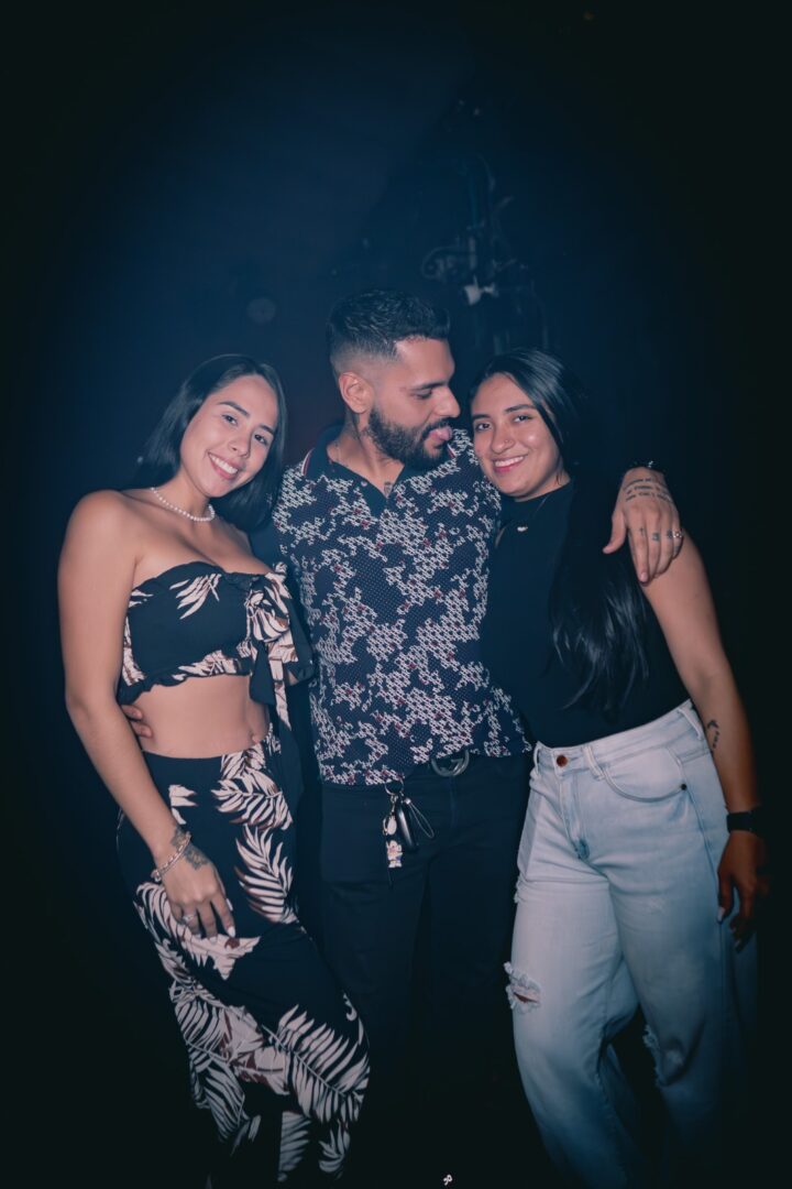 Three friends posing closely together at night.