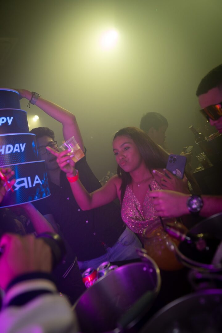 People celebrating a birthday in a dimly lit party with neon signs.