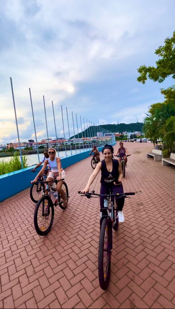 Group of friends biking along a waterfront promenade on a cloudy day.