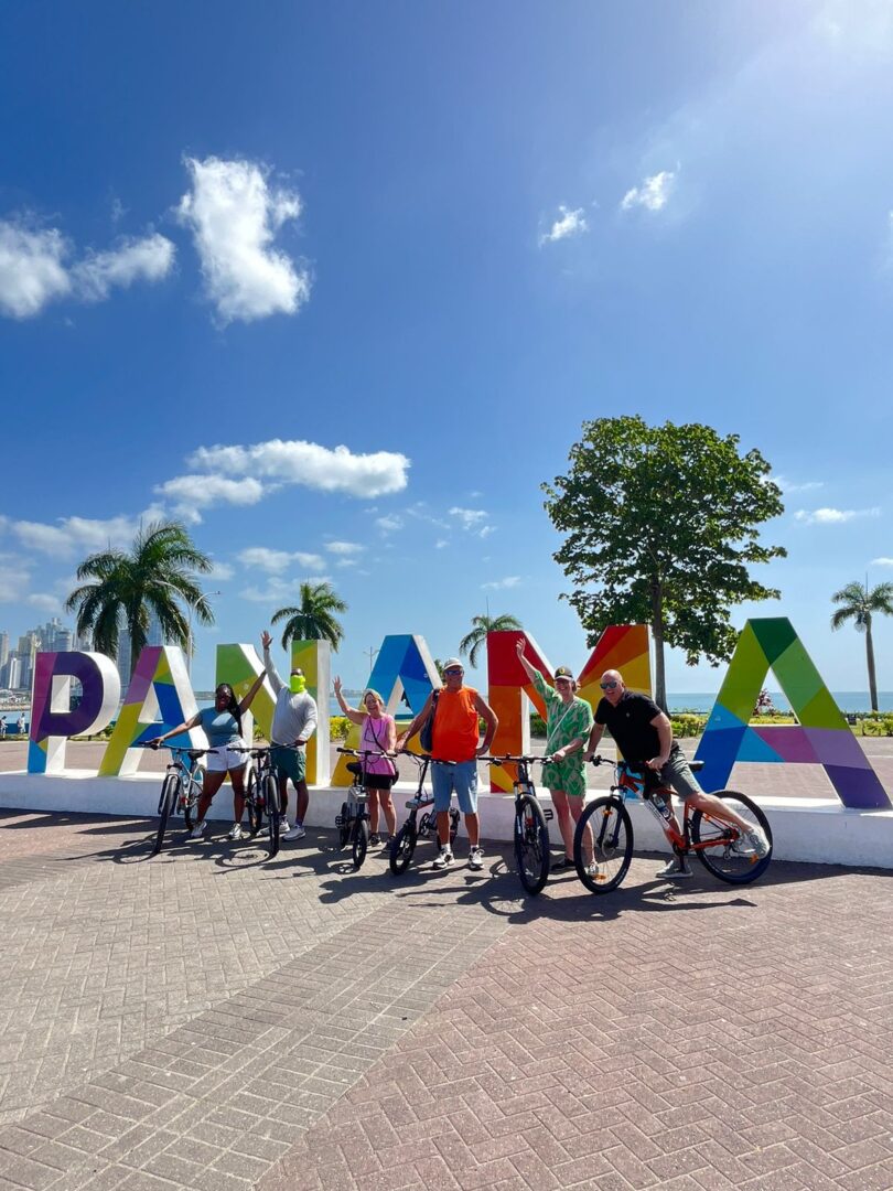 Cyclists posing in front of colorful Panama sign under a sunny sky.