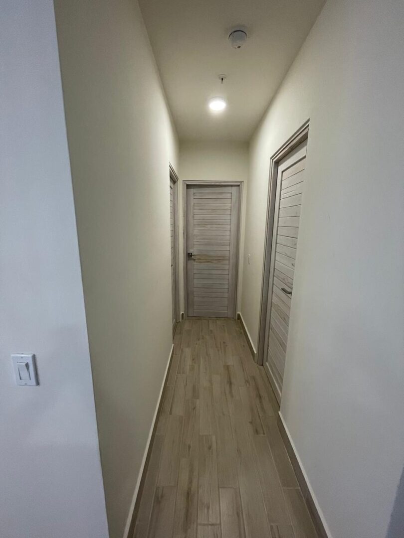 A narrow hallway with wooden flooring and closed white doors.