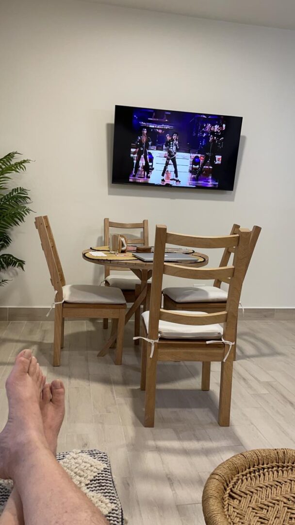 A cozy dining area with wooden chairs and a TV on the wall.