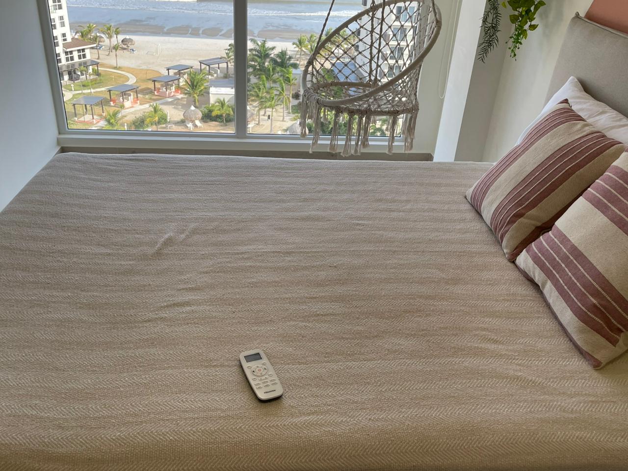 Remote control on a beige bed near a window with a view.