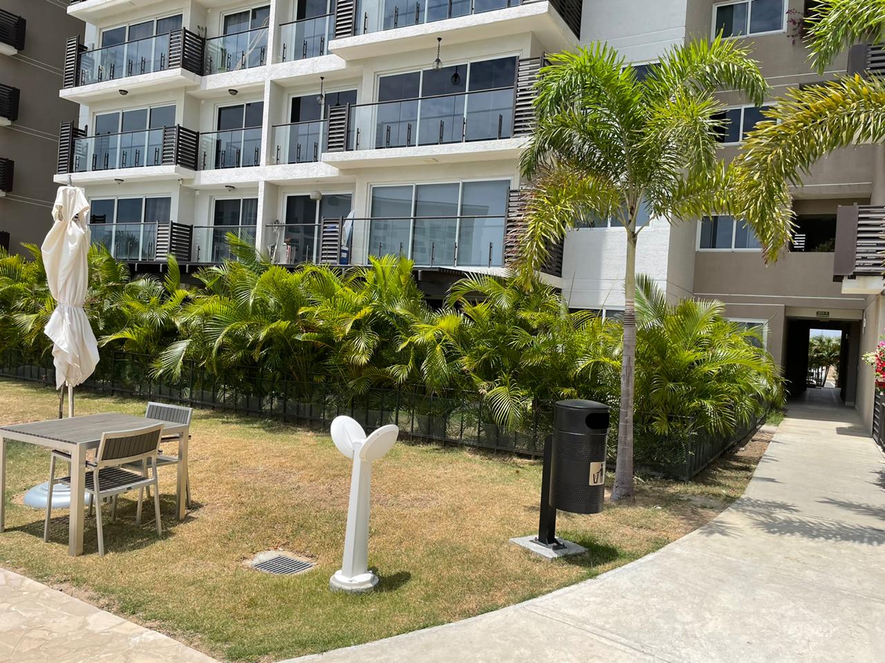 Outdoor patio area with tables, chairs, and tropical plants near a residential building.
