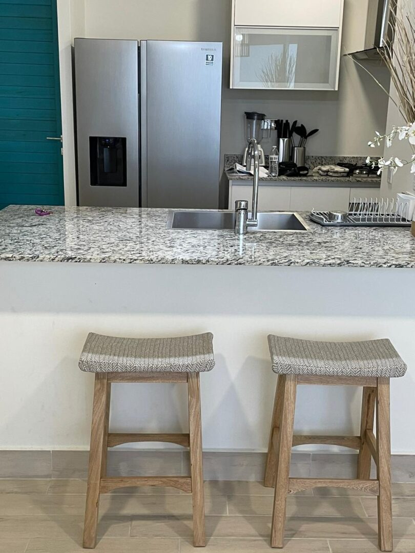 Two wooden stools with cushioned seats under a granite kitchen counter.